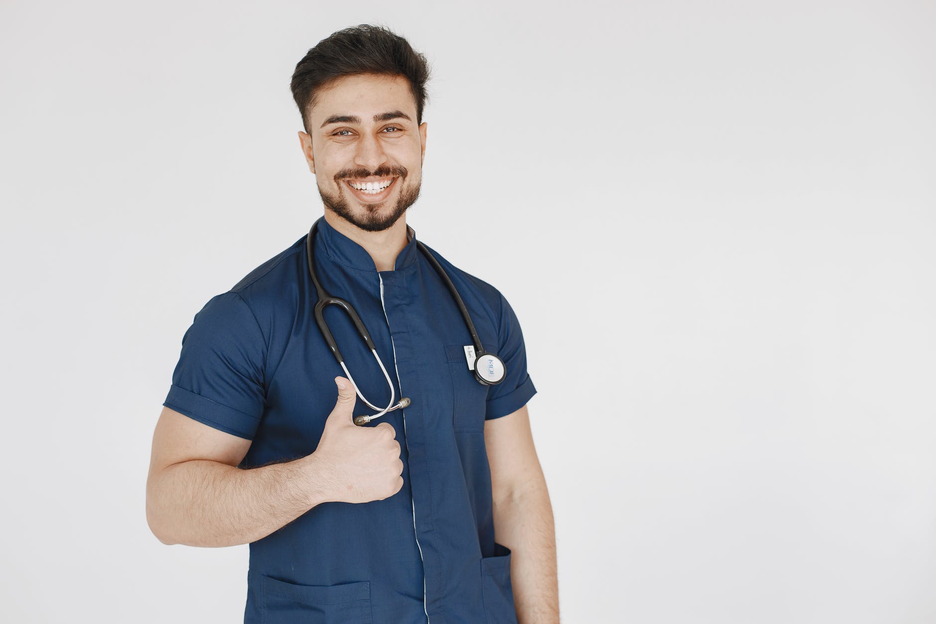 man in blue scrub suit with stethoscope doing a thumbs up hand sign